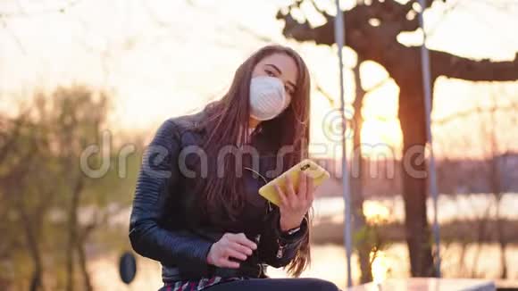 美丽的女性独自坐在公园里她用手机打电话她戴着保护面具以保护视频的预览图