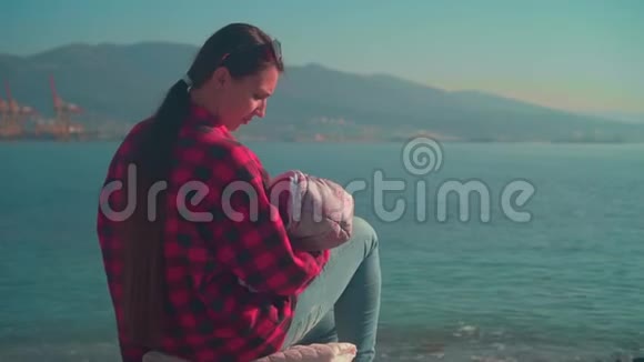 一位留着长发的年轻女子坐在海边抱着一个婴儿抱在大海的背景上视频的预览图