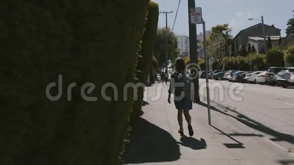 镜头跟随着快乐的年轻旅游女人背着背包沿着夏天的旧金山街道触摸着绿色的栅栏视频的预览图