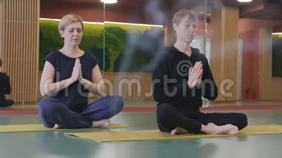 一个年轻人和一个女孩坐在莲花的位置在瑜伽工作室里冥想垫子一根香棒在抽烟视频的预览图