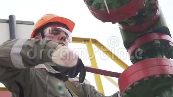 油工在橙色安全帽和防护玻璃开或关井口阀门关闭井石油减少视频的预览图