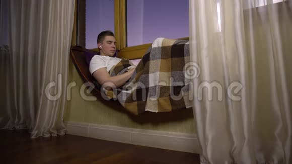 一个年轻人用耳机听音乐一个人躺在窗边的窗台上耳朵里戴着耳机视频的预览图