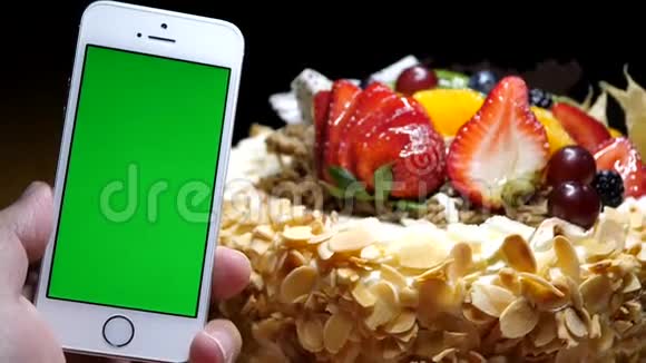 水果生日蛋糕和手拿绿色屏幕手机的动作视频的预览图