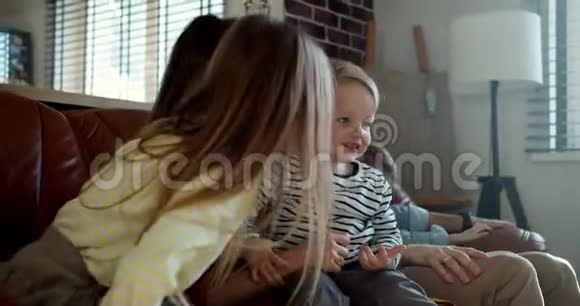 幸福的年轻家庭肖像白种人的父母和三个孩子在家中玩得很开心在沙发上慢动作视频的预览图