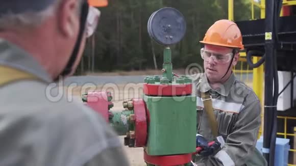 油工在橙色头盔和防护玻璃关闭阀的x质量井口关闭井石油减少视频的预览图