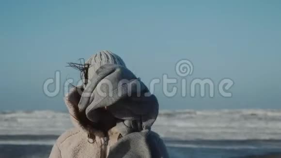 一幅美丽的欧洲旅游妇女在寒风中对着镜头微笑在寒冷的冬天海岸缓慢的运动视频的预览图