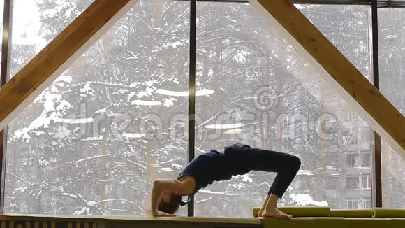 一个年轻可爱的家伙在一扇大窗户的窗台上做桥梁练习他做体操和瑜伽在外面视频的预览图