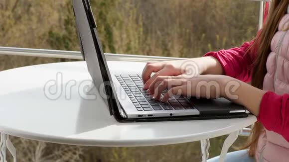 手在笔记本电脑键盘上打字的特写青少年女孩打字在笔记本电脑上工作在开放的阳台上春天阳光明媚视频的预览图
