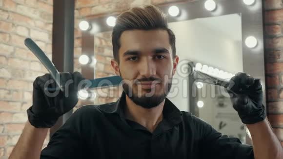 微笑的理发师在时尚理发店抢剪刀前摄像头用直剃刀使理发师眨眼的肖像视频的预览图