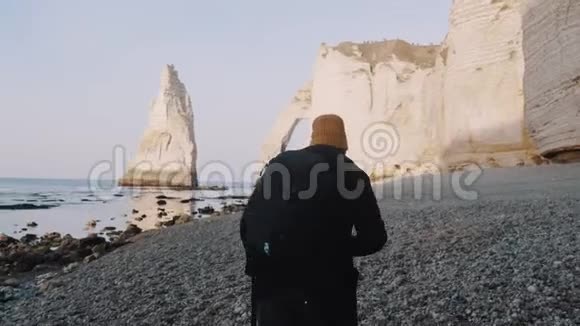 后景快乐的旅行者带着背包沿着阳光明媚的岩石海岸悬崖靠近埃特雷特诺曼迪慢动作视频的预览图
