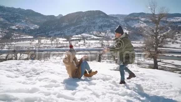 一对年轻漂亮的夫妇在一个阳光明媚的日子里在雪山上打雪球视频的预览图