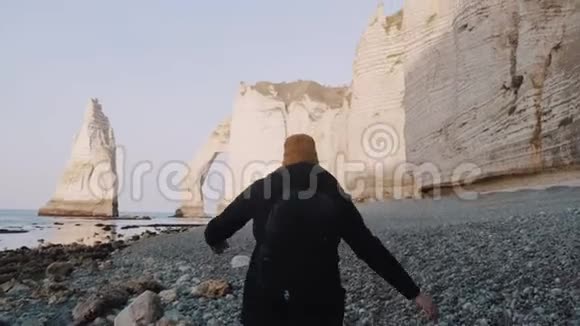 镜头跟随快乐的游客带着背包探索阳光明媚的岩石卵石海滩手臂张开在埃特雷特附近缓慢的运动视频的预览图