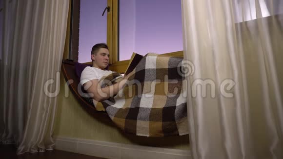 一个年轻人正在看书一个人躺在窗边的窗台上手里拿着一本书晚上出去视频的预览图