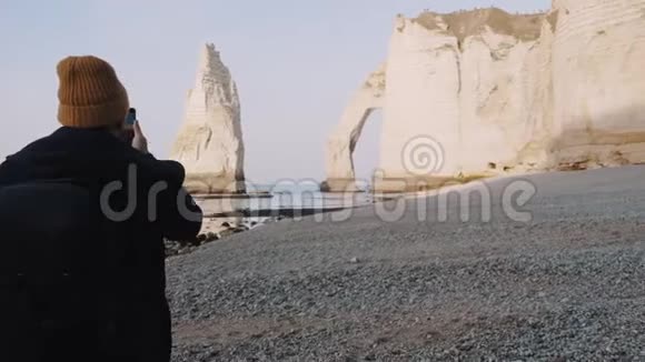 快乐男摄影师拍摄智能手机照片走向著名的Etretat海边白色悬崖拱门慢动作视频的预览图