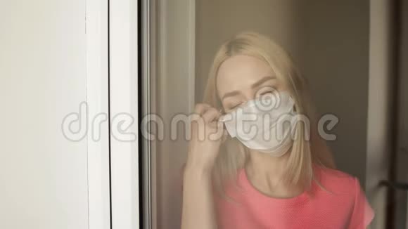 年轻漂亮的女孩摘下一个站在窗口的医疗面具视频的预览图