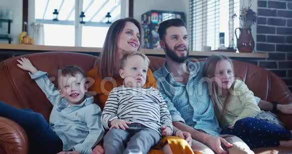 快乐的年轻白种人家庭的肖像有三个可爱的孩子在家里看电视一起在沙发上慢动作视频的预览图