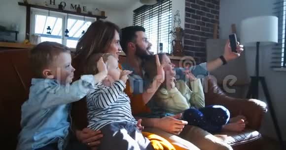 快乐的年轻白种人家庭与三个孩子挥手与朋友在智能手机视频通话在家里慢动作视频的预览图