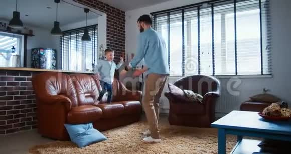 年轻快乐的白种人父亲和小儿子在现代轻屋客厅慢动作中尽情地拥抱和跳舞视频的预览图