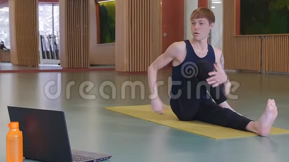 一位年轻的瑜伽老师在网上授课一个白人在笔记本电脑前的黄色垫子上锻炼视频的预览图