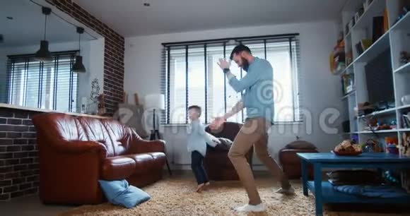 快乐的年轻白种人父亲和小儿子享受在轻盈的客厅里一起跳舞友谊概念慢动作视频的预览图