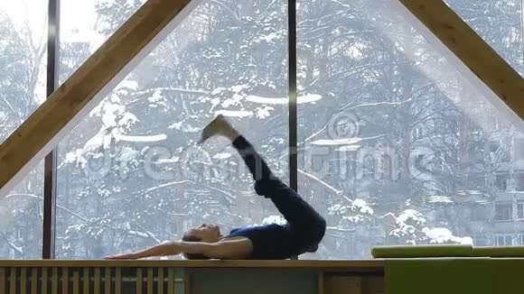 一个年轻人在一扇大窗户的窗台上做伸展运动和体操冬天在外面视频的预览图