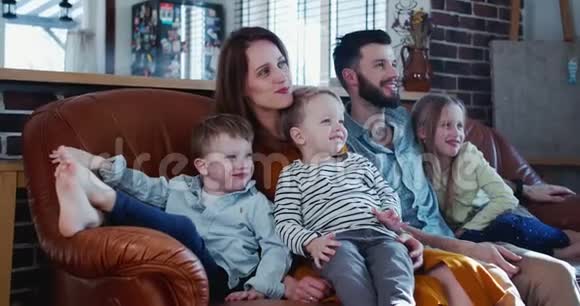 家庭时间在一起的概念快乐的年轻白种人父母和三个孩子在家看电视在沙发上慢动作视频的预览图