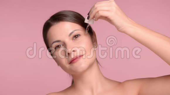 30多岁的黑发女人特写镜头拿着一个油滴在她的脸颊上放一些油穿一件脱褶上衣视频的预览图