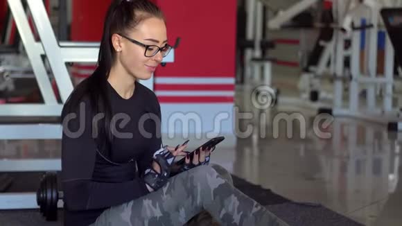 年轻女孩在健身房用智能手机视频的预览图
