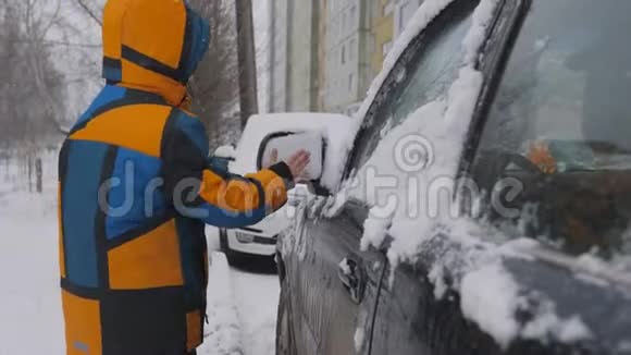 清理汽车侧窗积雪一个孩子在雪地上清洗后视镜一个孩子手清洁视频的预览图