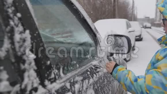 清理汽车侧窗积雪一个孩子在雪地上清洗后视镜一个孩子手清洁视频的预览图