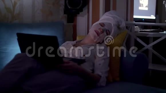 肖像女人戴着化妆面料面具头上戴着白色毛巾在笔记本电脑屏幕前睡着了视频的预览图