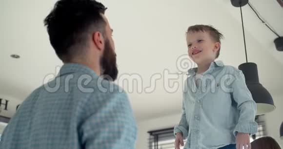 欢快可爱的小男孩开心的叫喊着跳进小爸爸怀里在家家庭时间慢动作视频的预览图