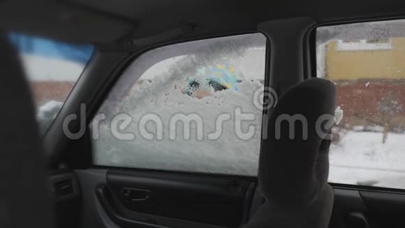 清理汽车侧窗积雪一个孩子手清洁汽车玻璃男孩笑得甜甜的视频的预览图
