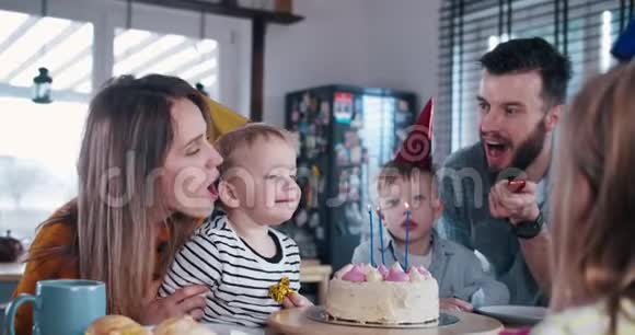 可爱的3岁白种人男孩孩子吹生日蛋糕在有趣的家庭聚会与纸屑慢动作视频的预览图