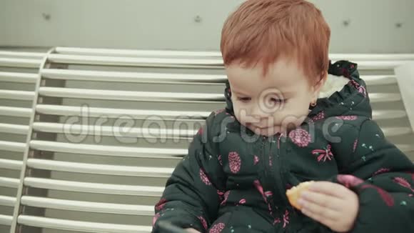 坐在白凳上吃饼干的红发小女孩视频的预览图