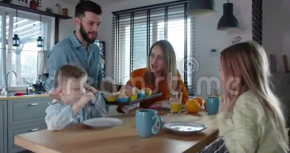 快乐的家庭时光理念小爸爸带来节日松饼与妈妈和可爱的孩子一起庆祝慢动作视频的预览图
