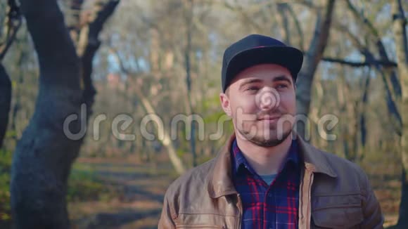 秋天公园里的年轻人穿着皮夹克和棒球帽的人看向别处他的背景是视频的预览图