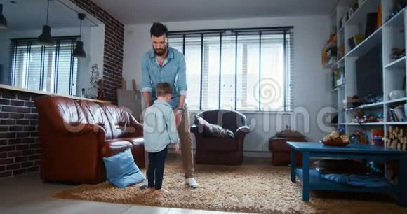 快乐的年轻白种人父亲和小儿子在现代轻屋客厅里玩耍拥抱和跳舞慢动作视频的预览图