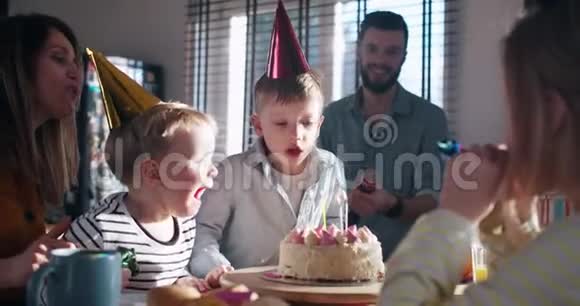 小快乐的白人男孩许愿在惊喜的家庭聚会上用五彩纸屑慢动作吹生日蛋糕视频的预览图