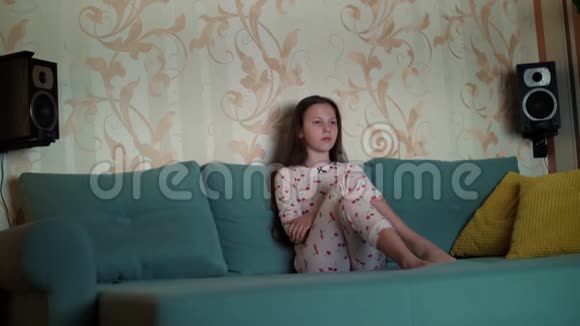 穿着睡衣在电视上看电影的少女坐在沙发上房间被来自视频的预览图