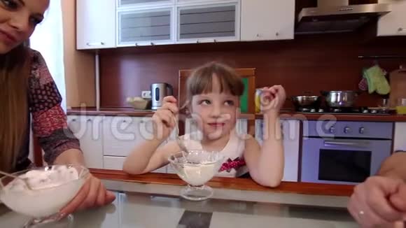 微笑的家人在家厨房吃冰淇淋可爱的小女孩在厨房的碗里吃冰淇淋视频的预览图