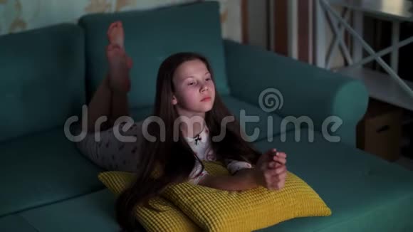 穿着睡衣在电视上看电影的十几岁女孩躺在沙发上房间被来自视频的预览图