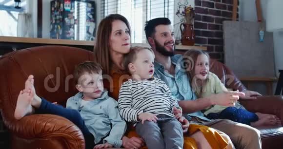 开朗快乐的年轻白种人家庭有三个可爱的孩子笑着在家里看电影在沙发上慢动作视频的预览图