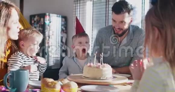 可爱的小白种人男孩许愿在家庭聚会上吹生日蛋糕蜡烛用纸屑慢动作视频的预览图
