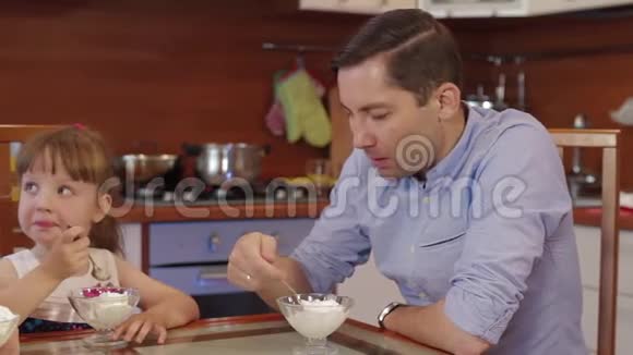 父母和女儿在厨房在家聊天吃冰淇淋可爱的小女孩在碗里吃冰淇淋视频的预览图