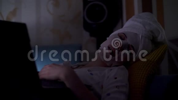 肖像女人戴着化妆面料面具头上戴着白色毛巾在笔记本电脑屏幕前睡着了视频的预览图
