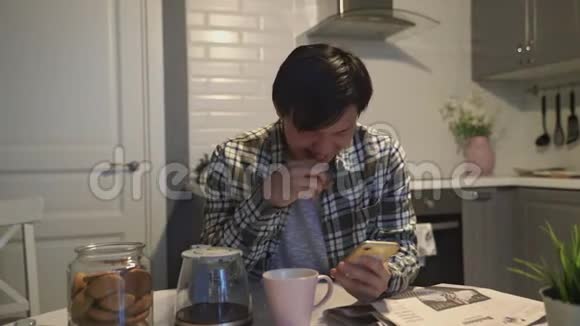 快乐的亚洲男人在智能手机上读一些有趣的东西在家厨房里笑视频的预览图