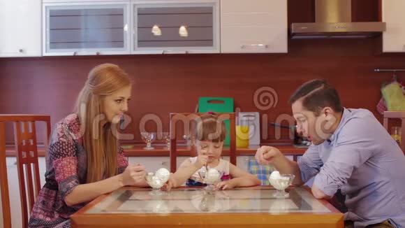 父母和女儿在家厨房吃冰淇淋可爱的小女孩在厨房的碗里吃冰淇淋视频的预览图