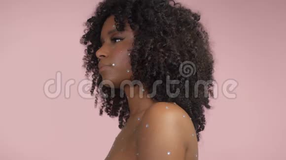 混合种族的黑人妇女卷发被水晶化妆覆盖在粉红色背景的工作室视频的预览图