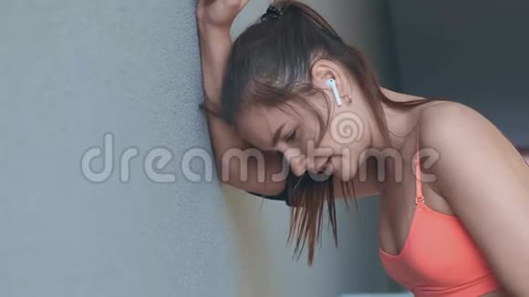 跑步后戴着耳机的疲惫女士靠在灰色的墙上视频的预览图